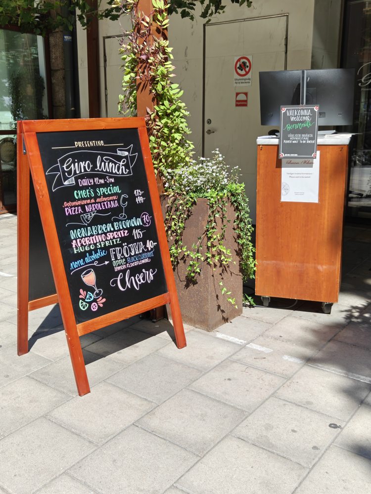 Orange-framed hand-lettered pavement sign outside a shop