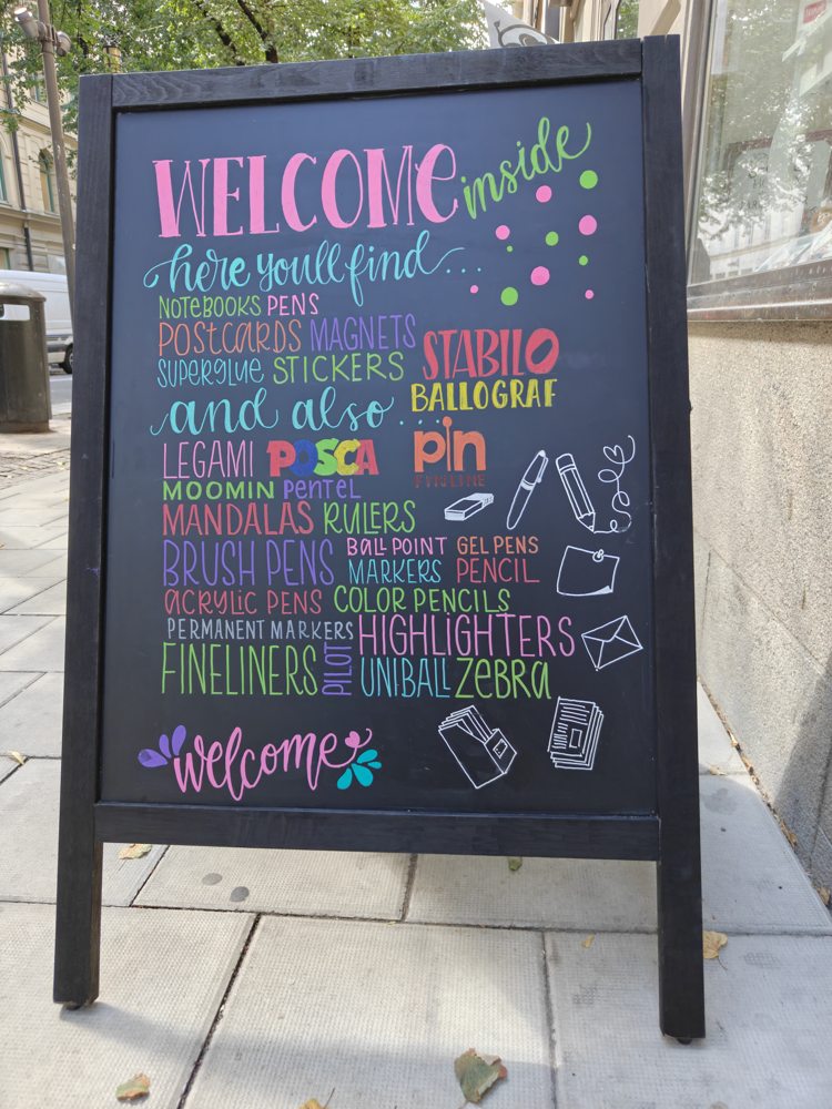 Black-framed pavement sign with colourful Welcome lettering and art-supply names
